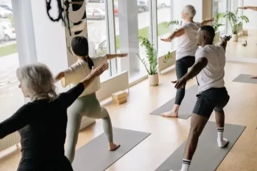 Des hommes et des femmes pratiquent le yoga dans une salle de cours collectifs.