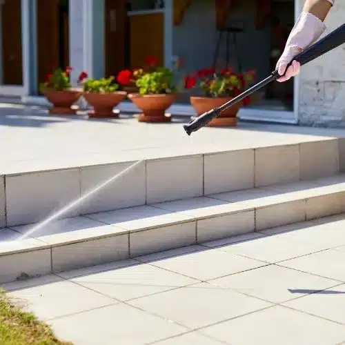 Une personne nettoie une terrasse au jet haute pression.