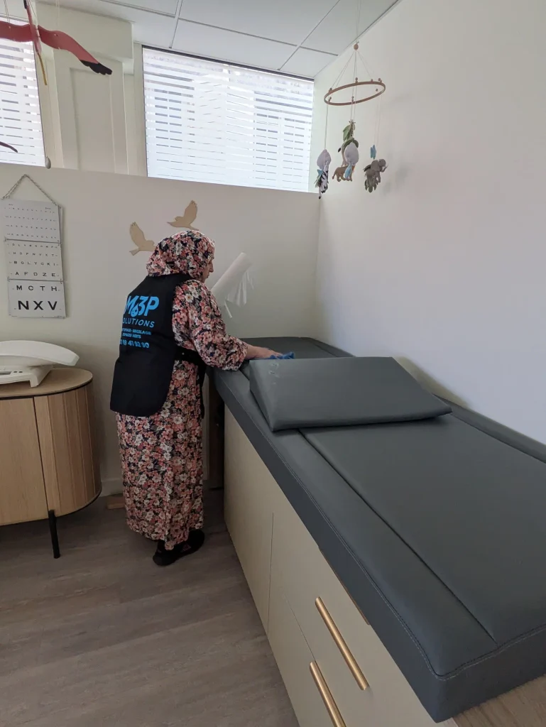 Une salariée M3P Solution désinfecte la table de consultation d'un docteur.